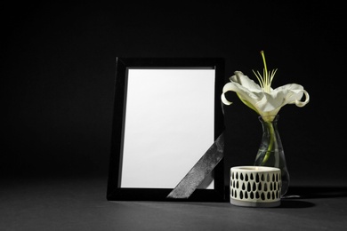 Funeral photo frame with ribbon, white lily and candle on black background. Space for design