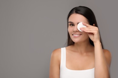 Photo of Young woman cleaning her face with cotton pad on grey background. Space for text