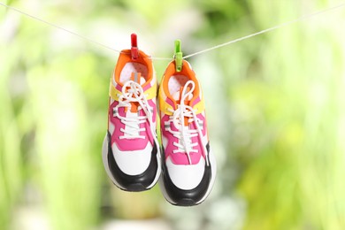 Photo of Stylish sneakers drying on washing line against blurred background