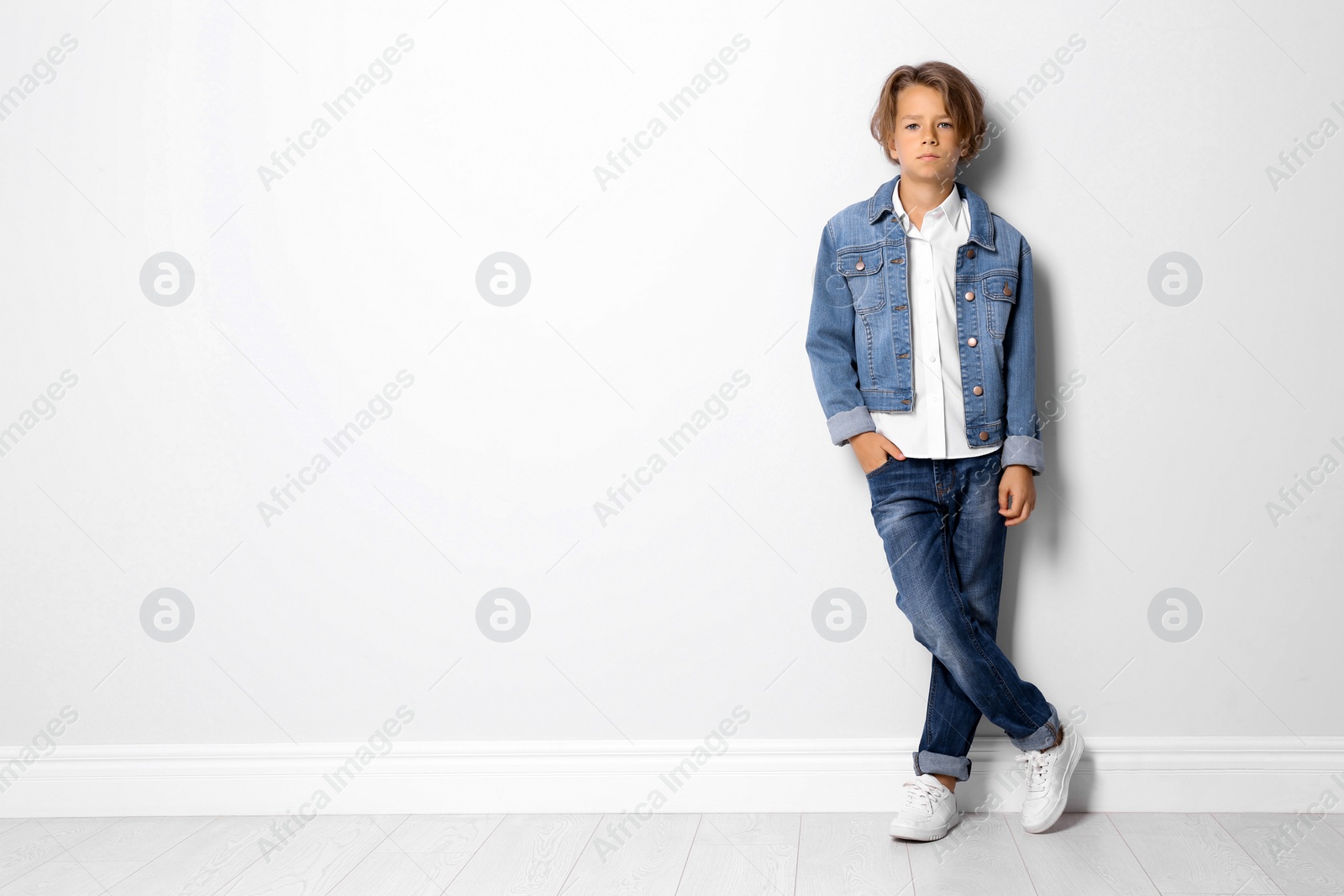 Photo of Cute little boy in casual outfit near white wall. Space for text