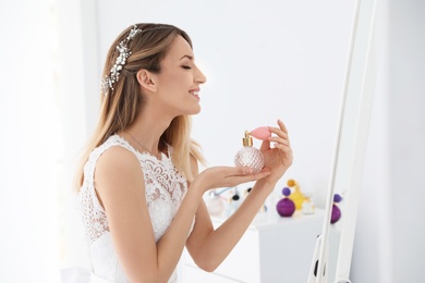 Photo of Beautiful young bride with bottle of perfume near mirror indoors