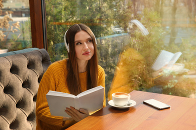 Photo of Woman listening to audiobook at table in cafe