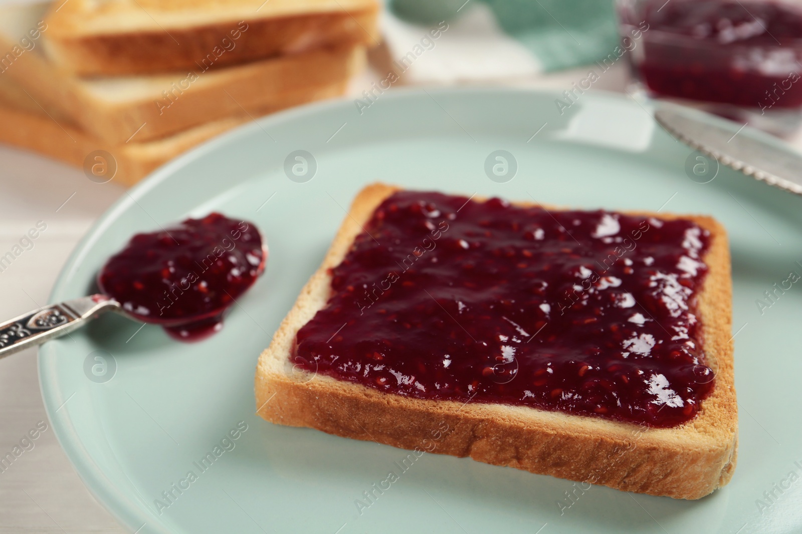 Photo of Toast with tasty raspberry jam and spoon on plate, closeup