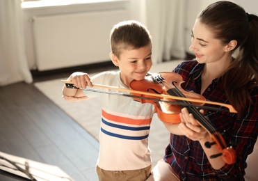 Young woman teaching little boy to play violin indoors