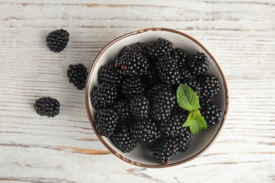 Bowl of ripe blackberries with mint on white wooden table, top view
