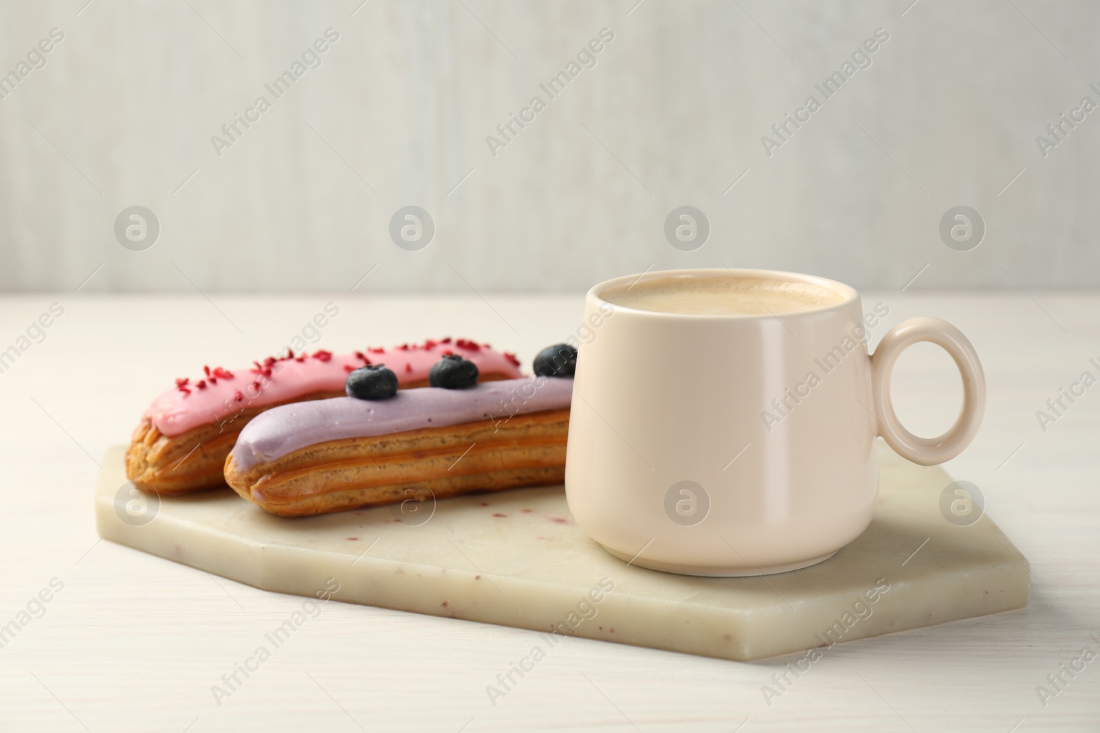 Photo of Cup of coffee and delicious eclairs covered with glaze on white wooden table