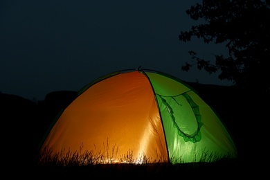 Photo of Modern tent lit from inside in wilderness at night. Overnight camping