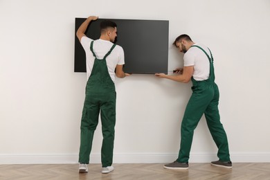 Photo of Professional technicians with screwdriver installing modern flat screen TV on wall indoors