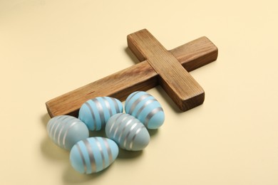 Wooden cross and painted Easter eggs on beige background