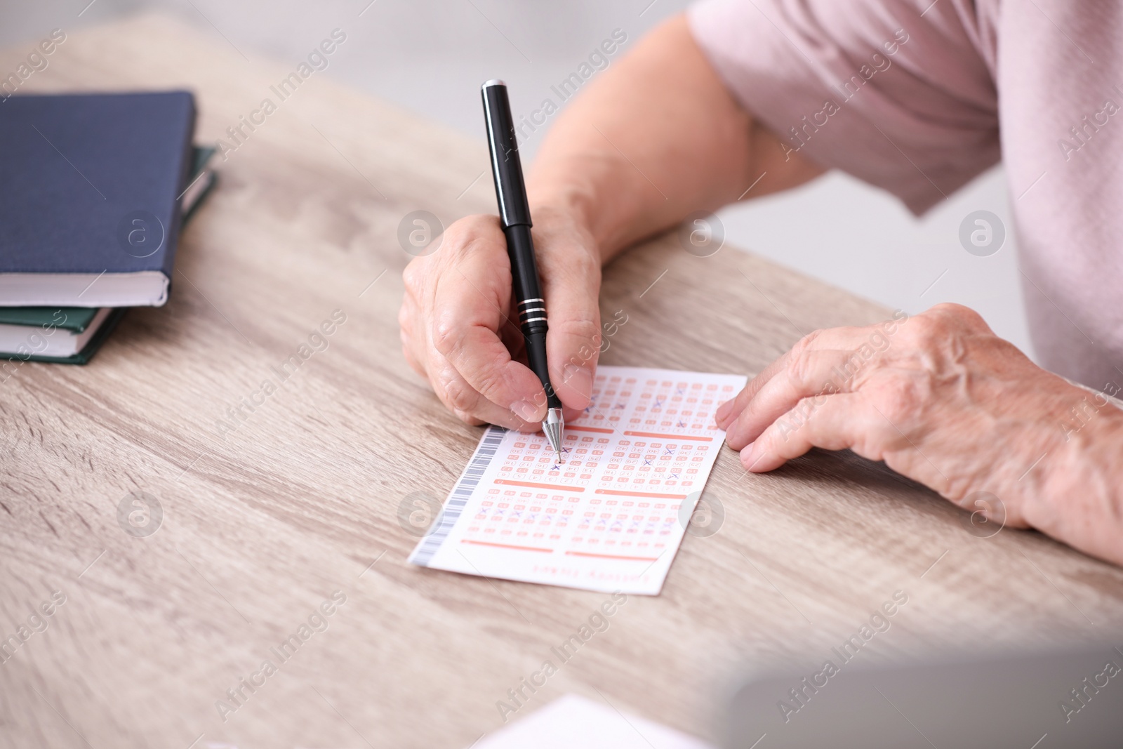 Photo of Senior woman filling out lottery ticket at table, closeup