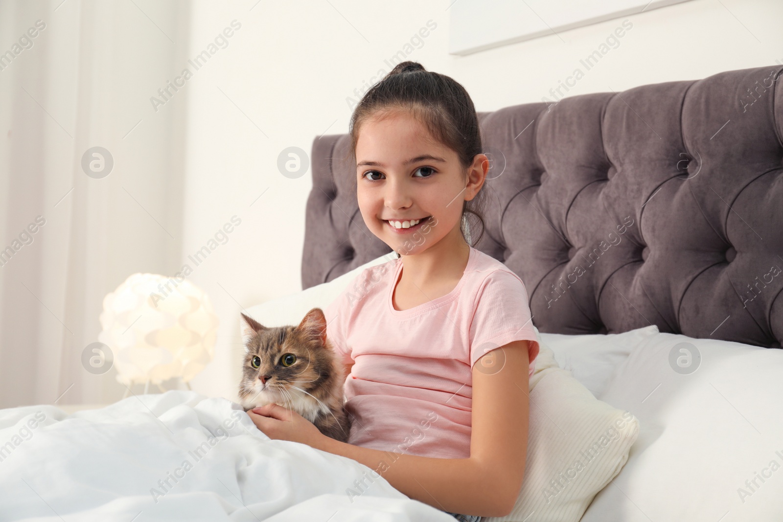 Photo of Cute little girl with cat lying in bed at home. First pet