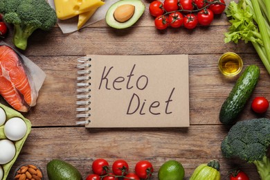 Photo of Notebook with phrase Keto Diet and different products on wooden table, flat lay