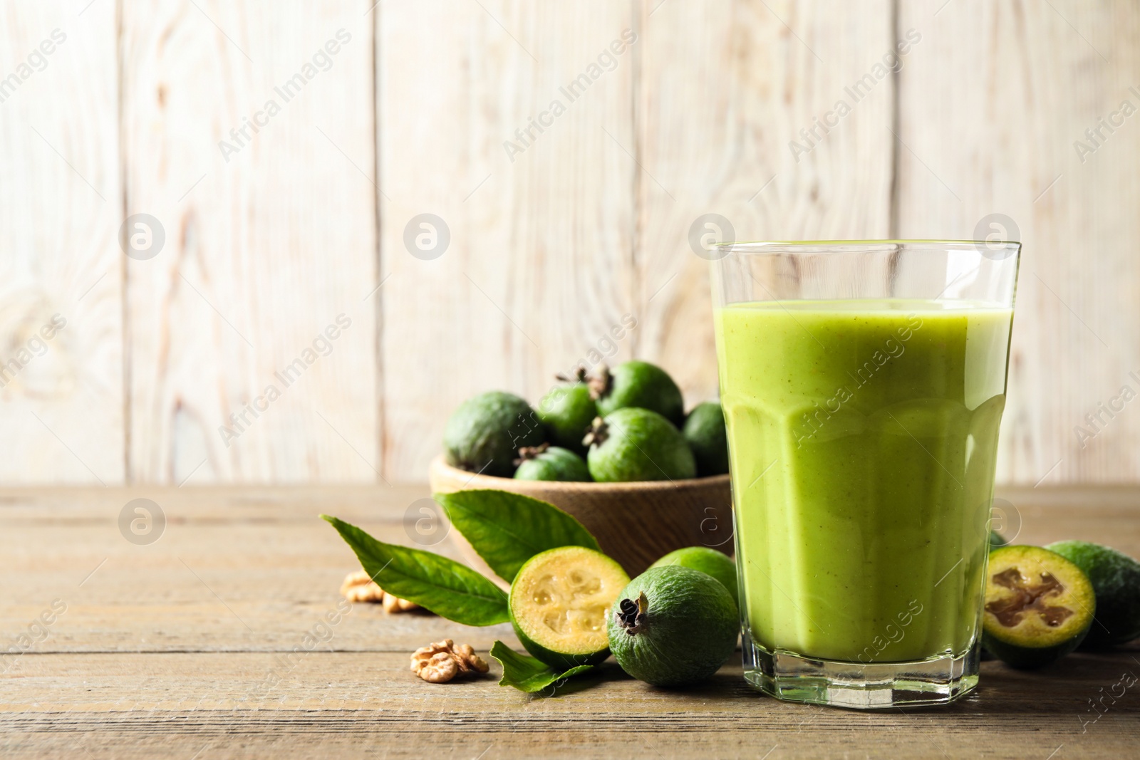 Photo of Fresh feijoa smoothie and fresh fruits on wooden table, closeup. Space for text