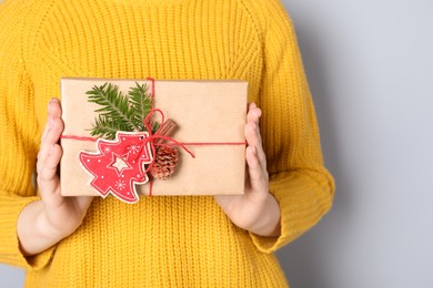 Photo of Woman holding beautifully wrapped Christmas gift box on light grey background, closeup. Space for text