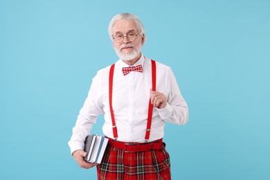 Portrait of stylish grandpa with glasses, bowtie and books on light blue background