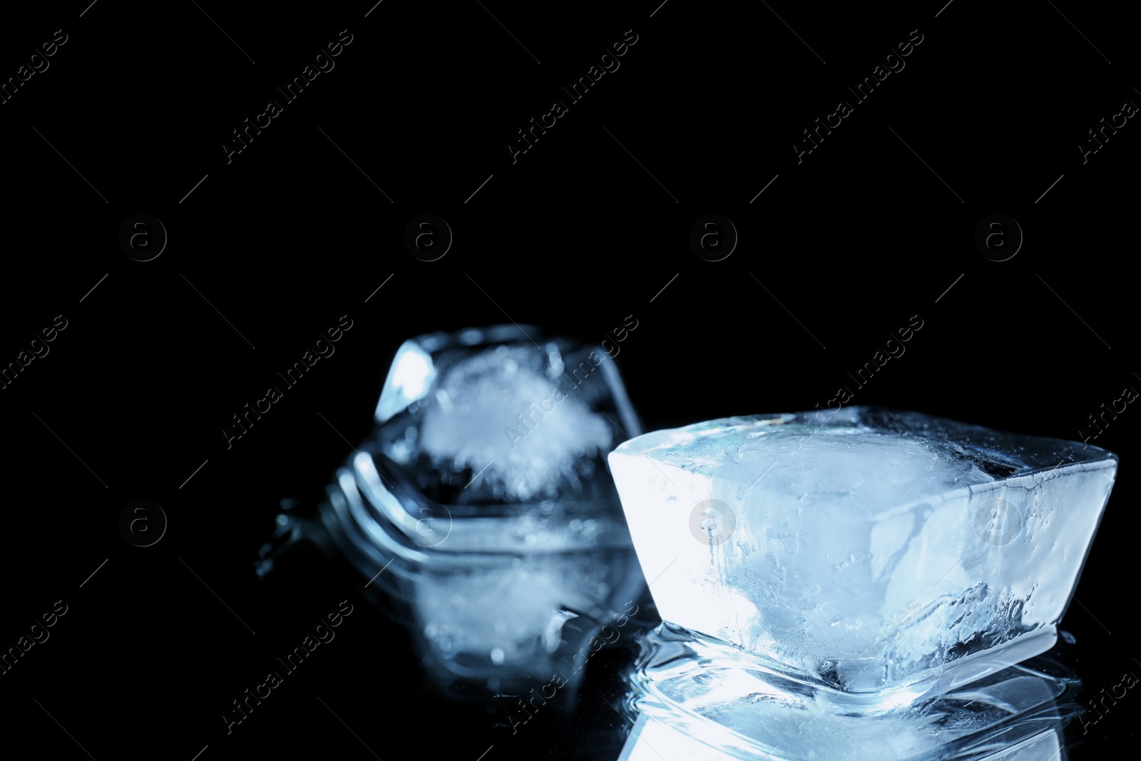 Photo of Transparent ice cube on black mirror surface. Space for text