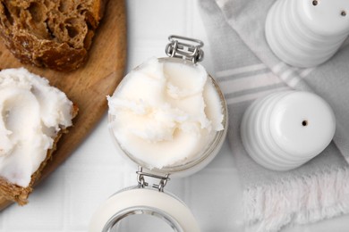 Photo of Delicious pork lard in glass jar, bread and spice shakers on white table, flat lay