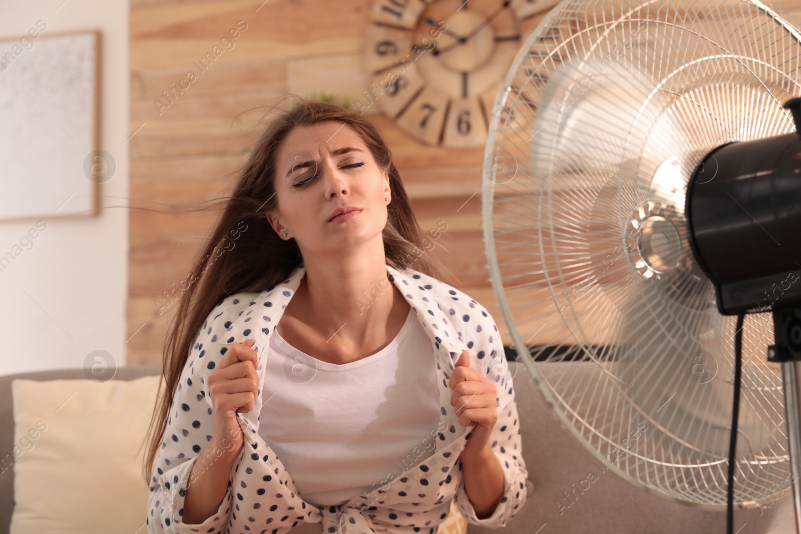 Photo of Woman enjoying air flow from fan on sofa in living room. Summer heat