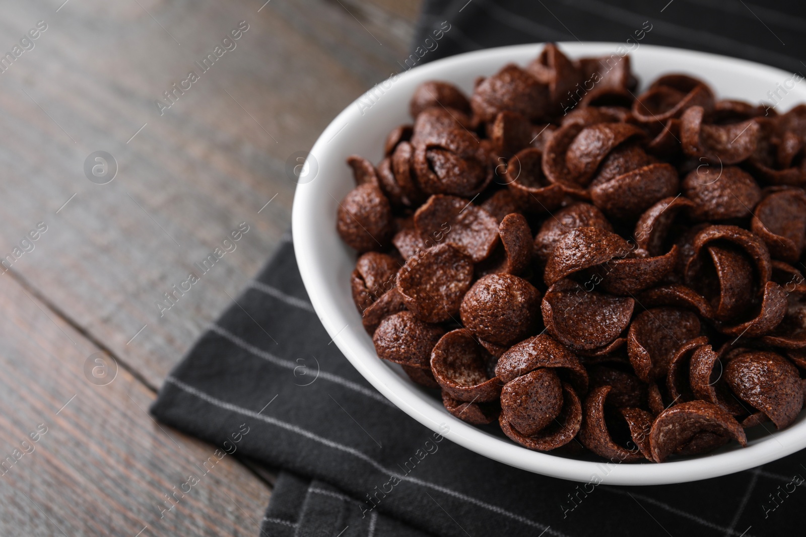 Photo of Breakfast cereal. Chocolate corn flakes in bowl on wooden table, closeup. Space for text