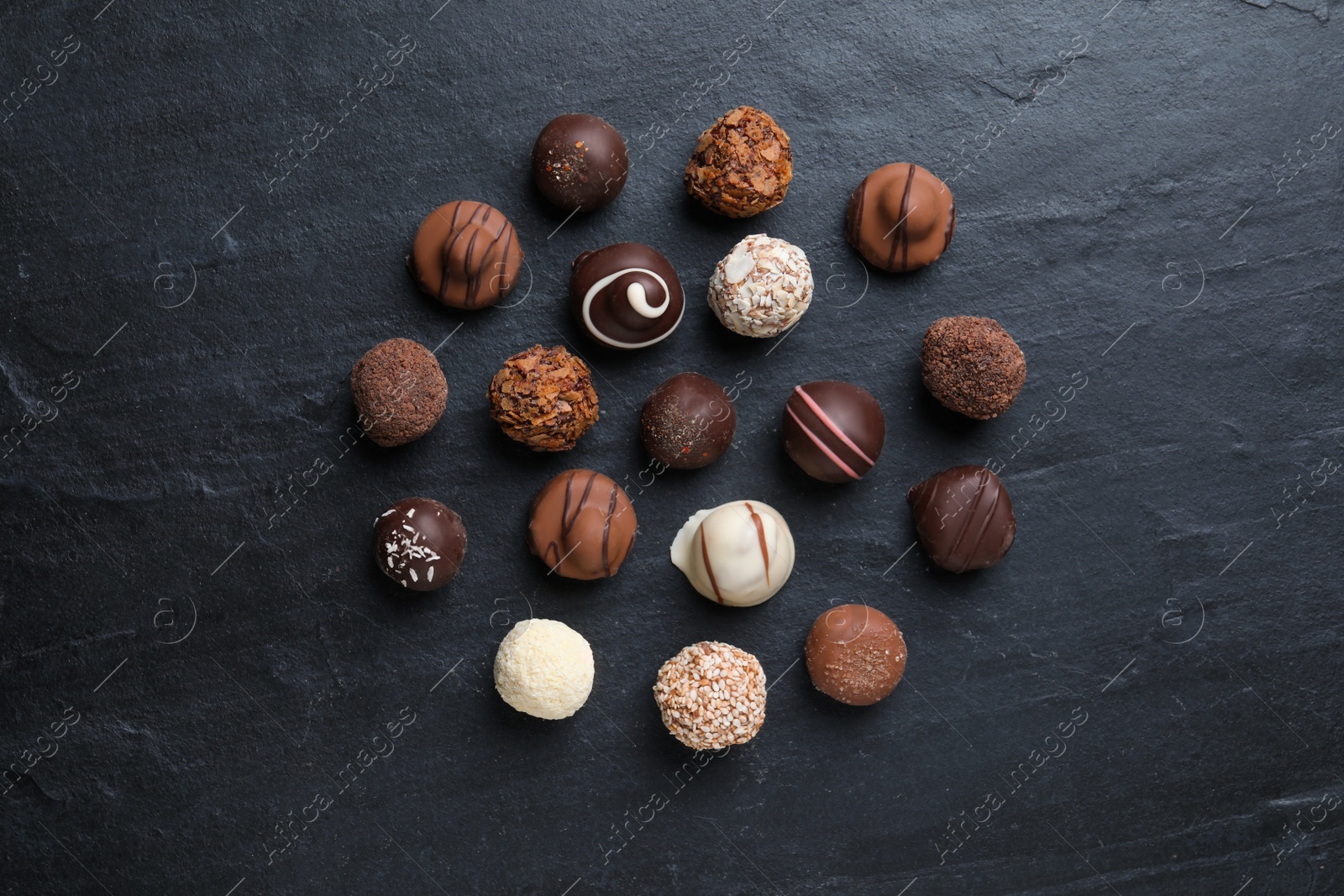 Photo of Different delicious chocolate candies on black table, flat lay