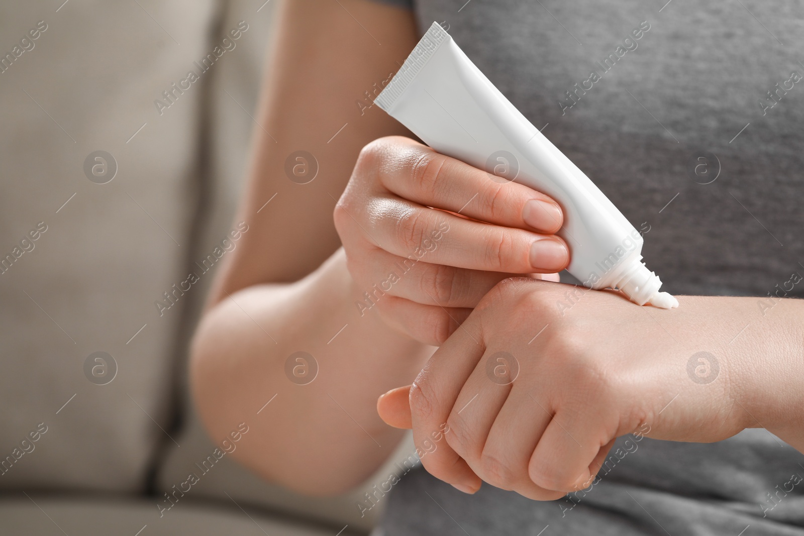 Photo of Woman applying ointment from tube onto her hand indoors, closeup