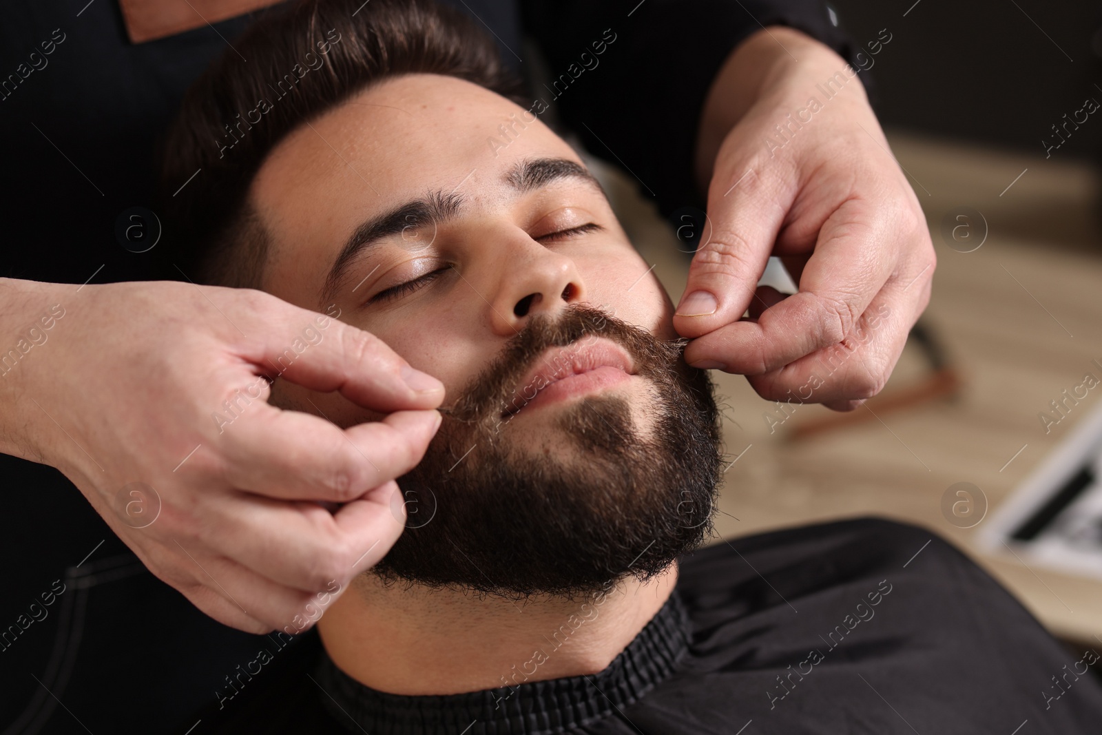 Photo of Professional barber working with client's mustache in barbershop, closeup