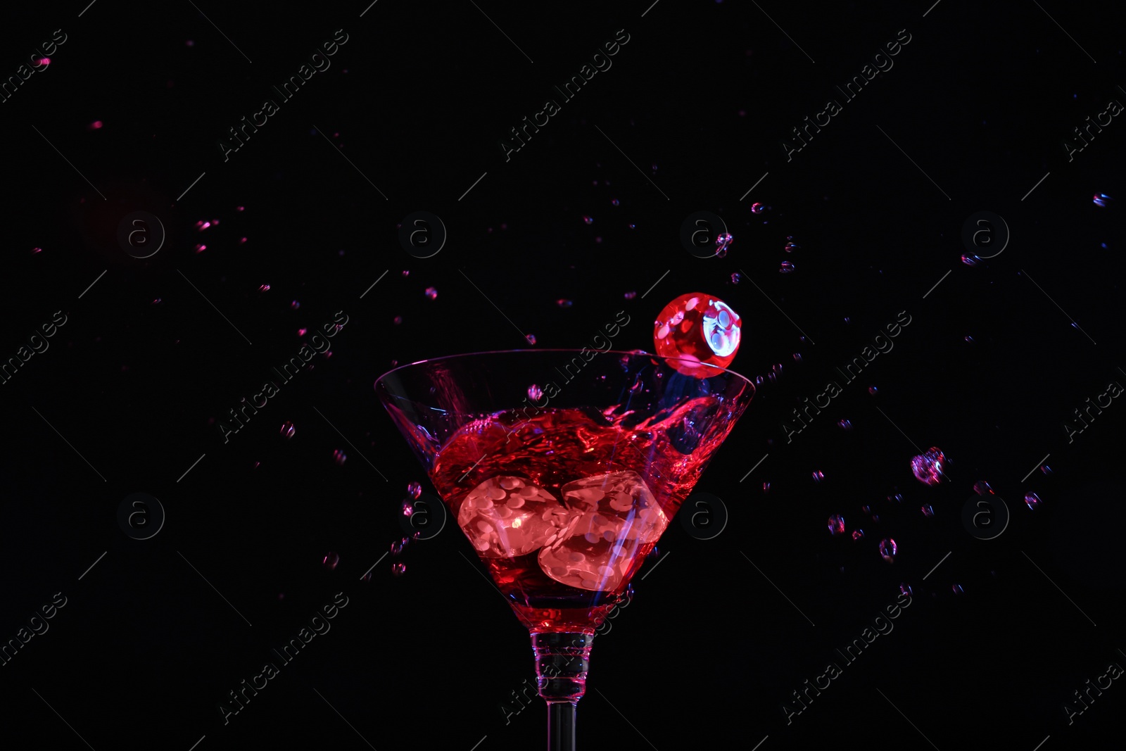 Photo of Casino dice falling into glass of alcohol drink on black background