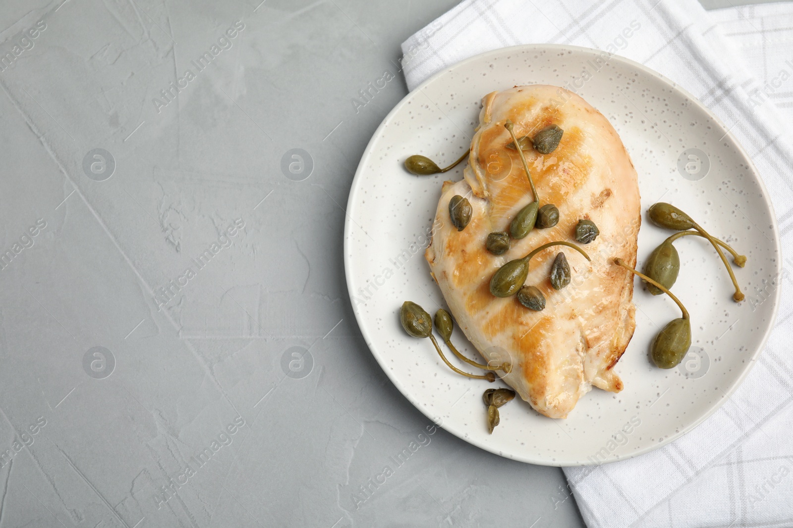 Photo of Delicious cooked chicken fillet with capers served on light grey table, top view. Space for text