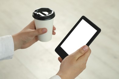 Photo of Man with cup of coffee using e-book reader indoors, closeup