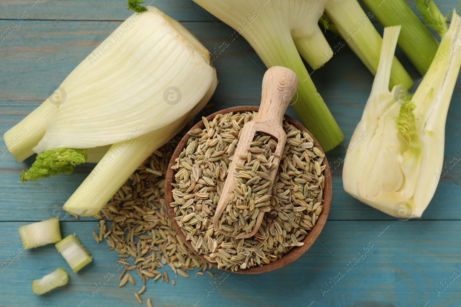 Photo of Fennel seeds in bowl, fresh vegetables and scoop on light blue wooden table, flat lay