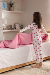Photo of Cute little girl making bed at home