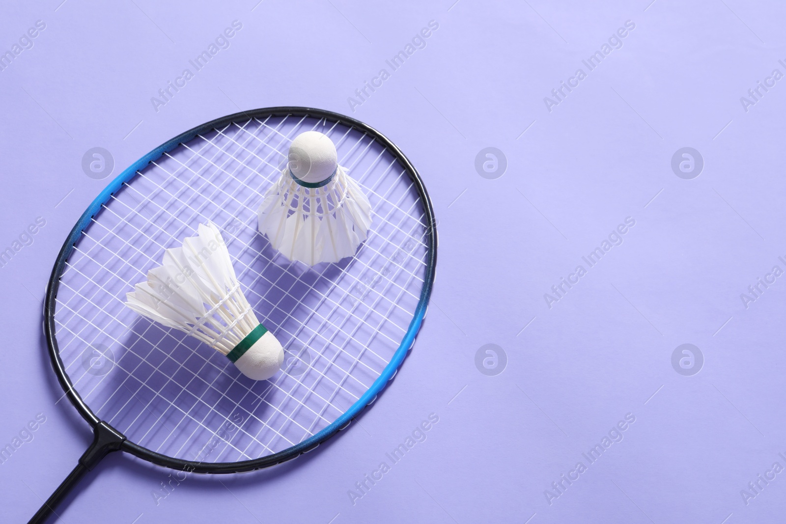 Photo of Feather badminton shuttlecocks and racket on violet background, above view. Space for text