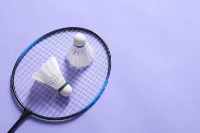 Feather badminton shuttlecocks and racket on violet background, above view. Space for text