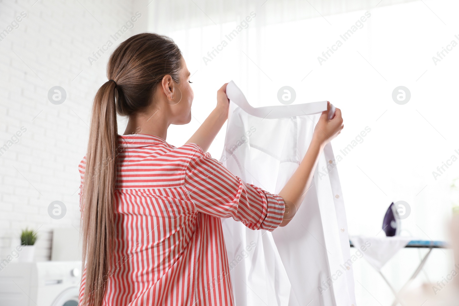 Photo of Young woman with clean shirt indoors. Laundry day