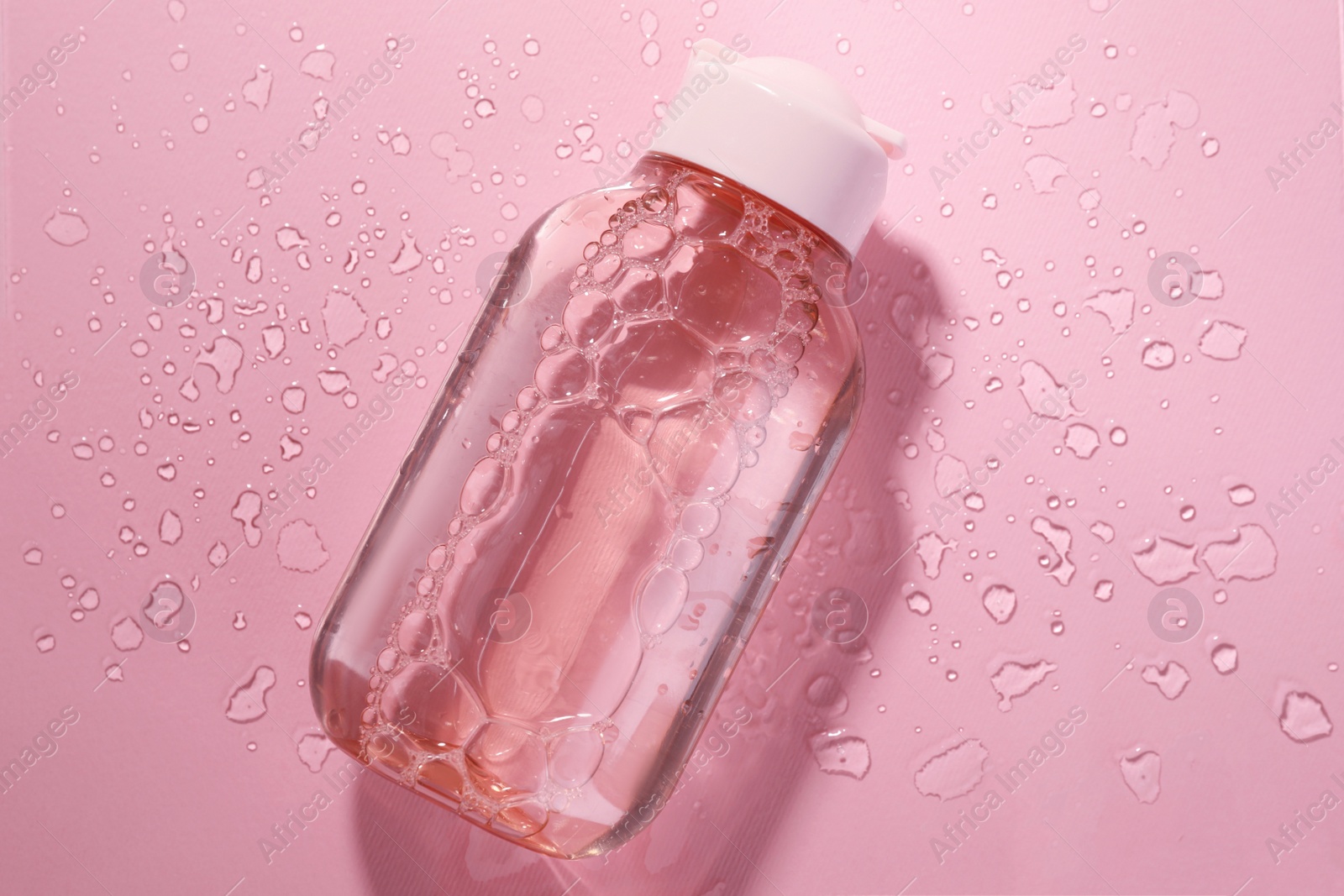 Photo of Wet bottle of micellar water on pink background, top view