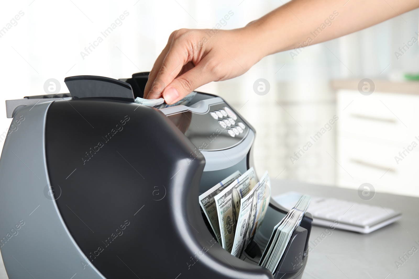 Photo of Woman putting money into counting machine at table indoors, closeup