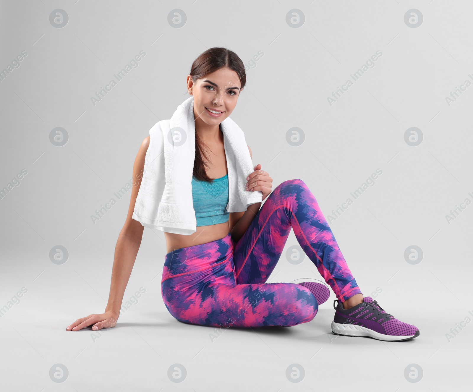 Photo of Beautiful young woman in sportswear with towel sitting on white background