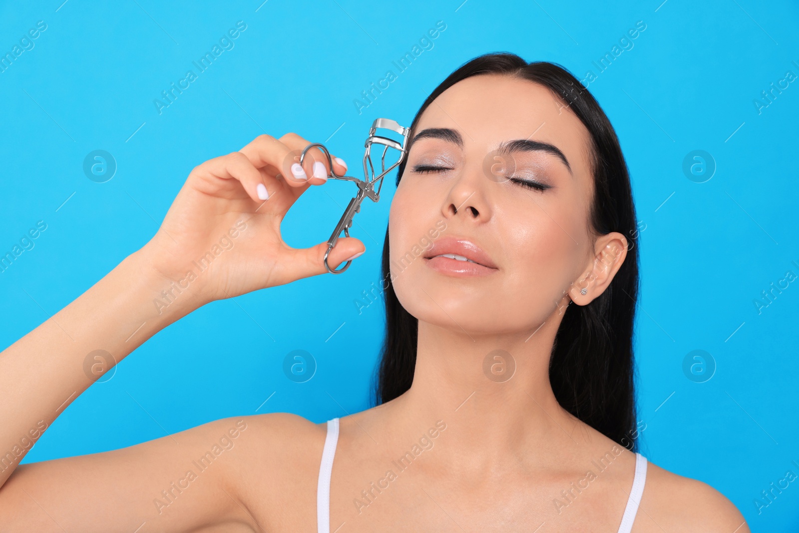 Photo of Beautiful young woman using eyelash curler on light blue background