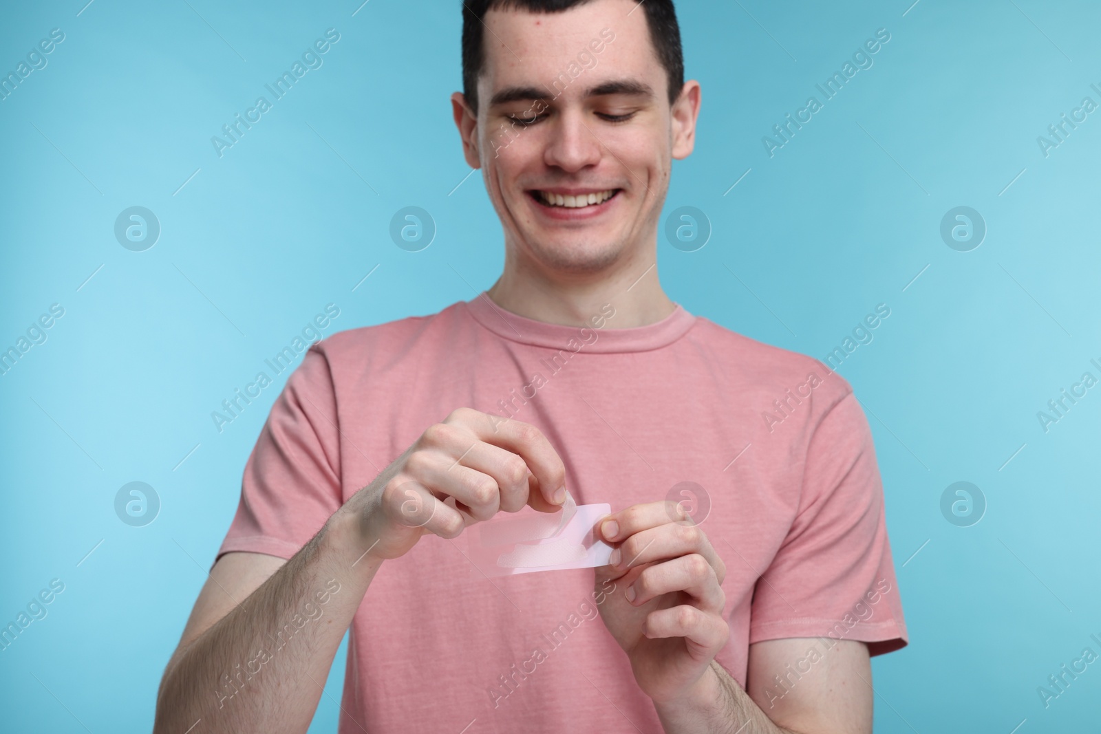 Photo of Young man with whitening strips on light blue background