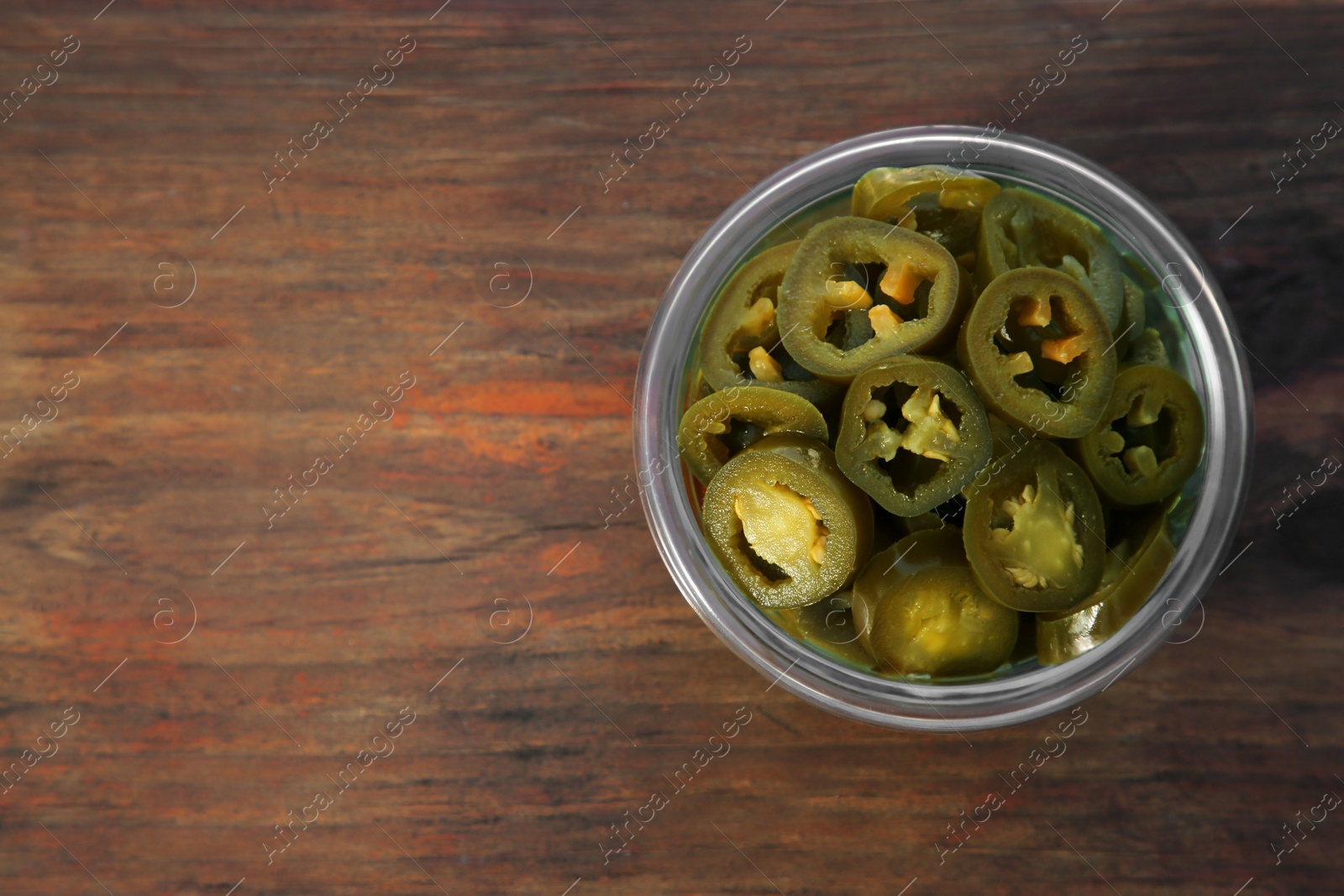 Photo of Glass jar of pickled green jalapeno peppers on wooden table, top view. Space for text