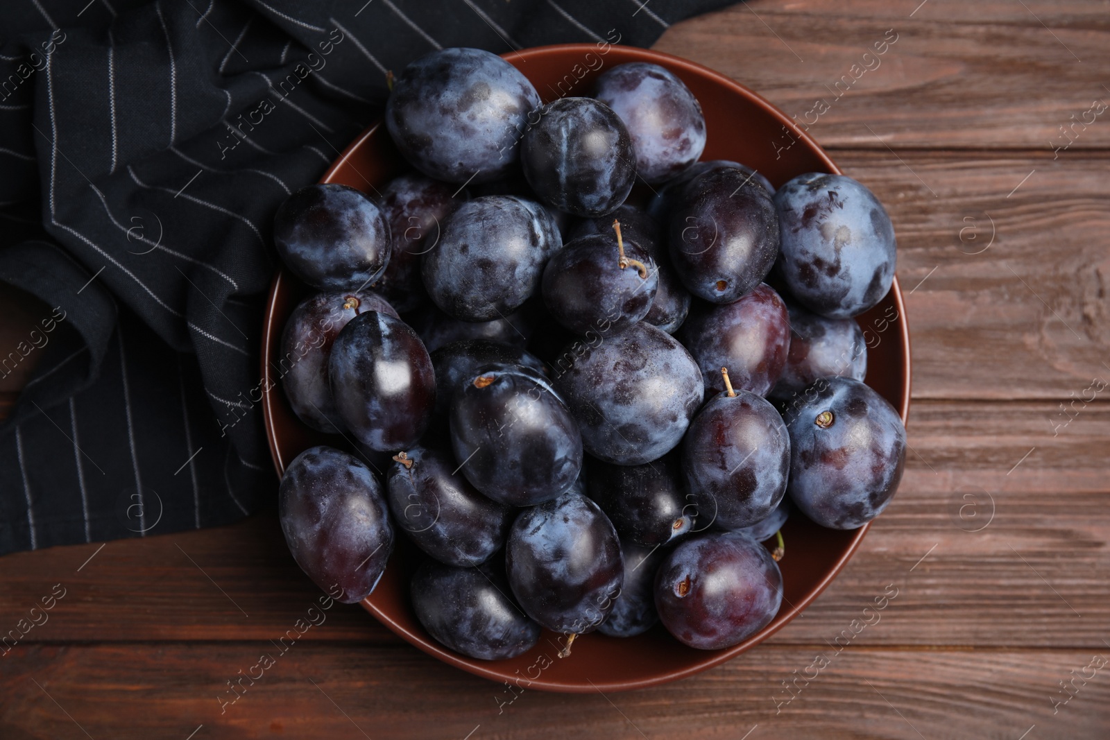 Photo of Delicious ripe plums in bowl on wooden table, top view