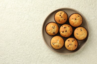 Photo of Delicious sweet muffins with chocolate chips on light textured table, top view. Space for text