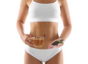 Young woman with fresh and dry leaves holding cup of diet tea on white background, closeup