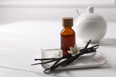 Photo of Vanilla pods, essential oil and flowers on white wooden table, space for text