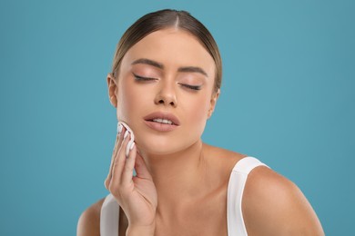 Photo of Beautiful woman removing makeup with cotton pad on light blue background