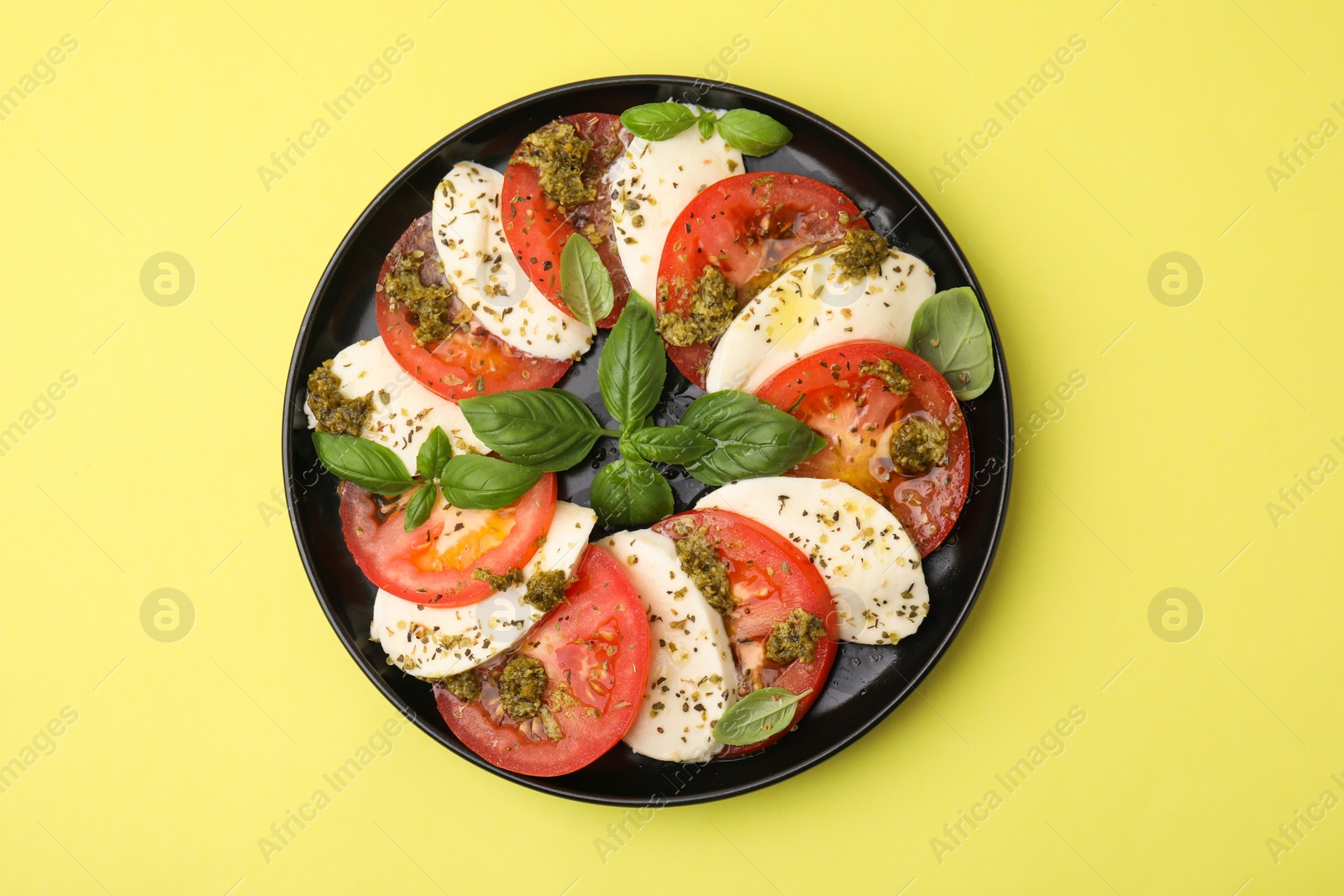 Photo of Plate of delicious Caprese salad with pesto sauce on yellow table, top view