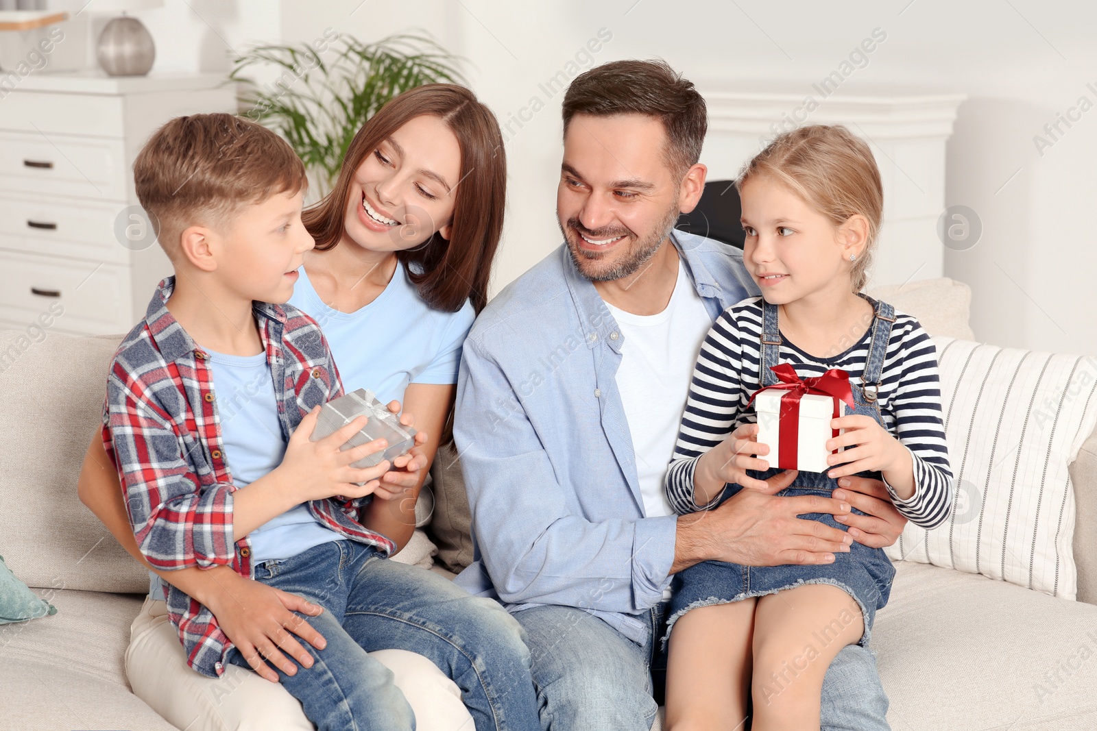 Photo of Happy family presenting each other with gifts on sofa at home