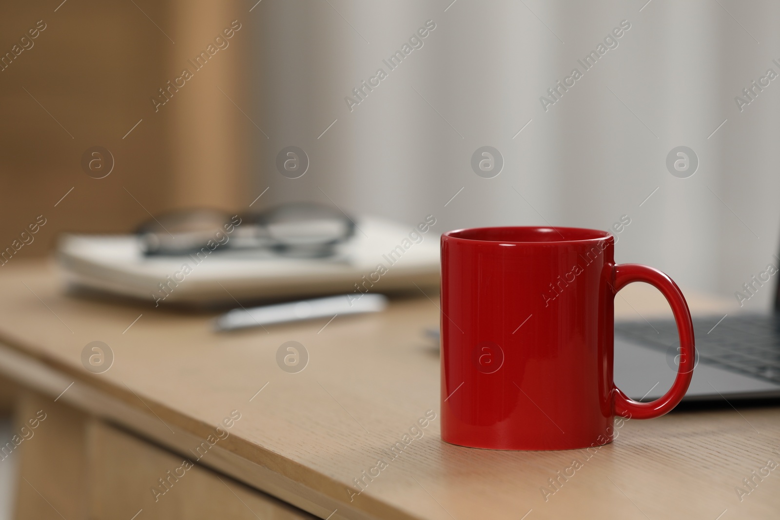 Photo of Red ceramic mug and laptop on wooden table at workplace. Space for text