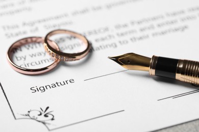 Photo of Marriage contract, fountain pen and wedding rings on table, closeup