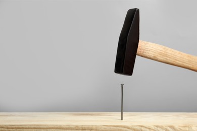 Photo of Hammering nail into wooden surface against grey  background, space for text